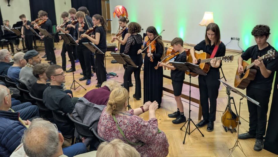 Young members of the Shropshire Music Service's Shropshire World Folk Ensemble, playing a variety of stringed instruments, performing on stage
