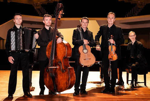 The five members of the quintet, holding their instruments and standing in a row on a stage with their backs to the concert hall seating