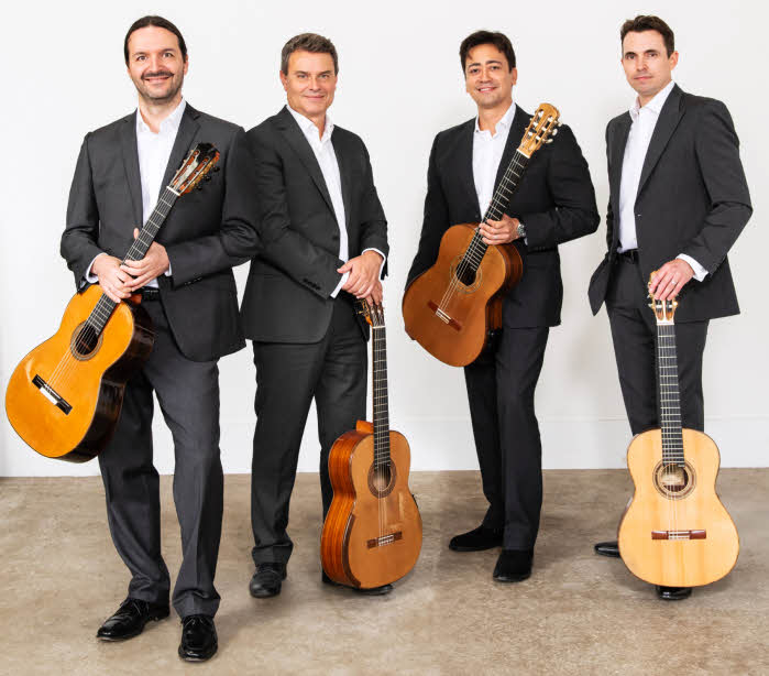 The quartet, standing holding their guitars