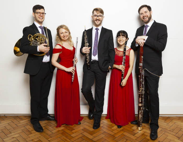 The quintet, standing with their instruments and similing happily