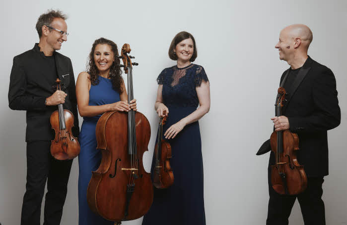 The quartet, standing with their instruments and similing happily